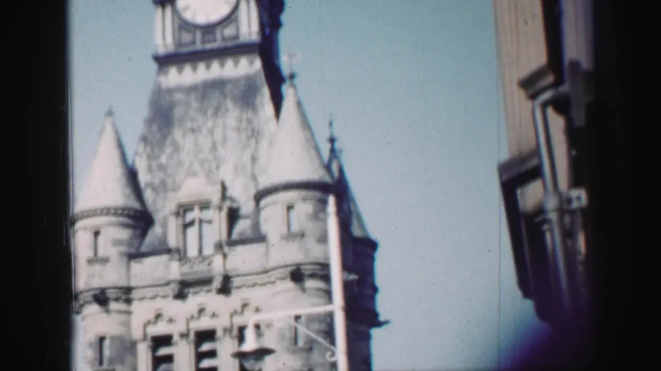 1952 Edinburgh frame showing the church tower rising to a visible clock face, with turrets and adjacent building edge.