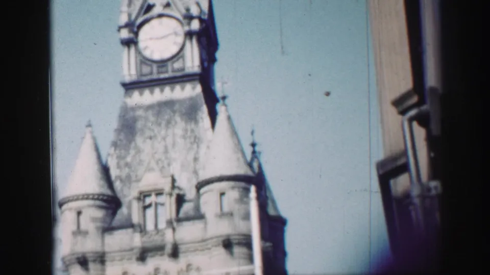 1952 Edinburgh home-movie frame showing a historic clock tower with turrets against pale blue sky, partly obscured by dark framing.