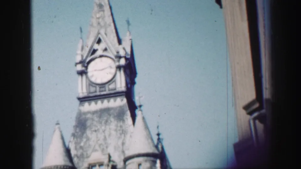 1952 Edinburgh travel footage frame with the clock tower centered near a dark window or building edge under clear sky.