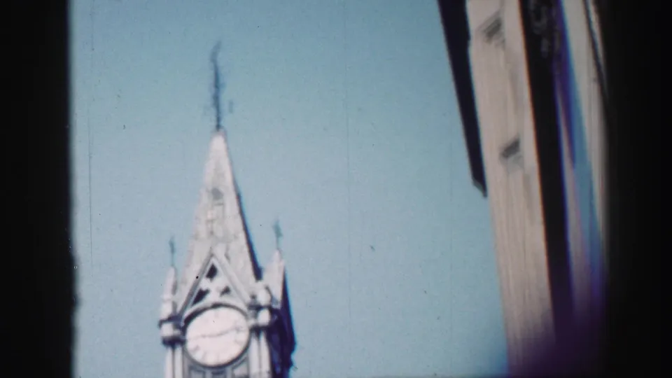 Handheld 8mm frame from Edinburgh showing the pointed clock tower cropped low in the frame beside a dark vertical obstruction.
