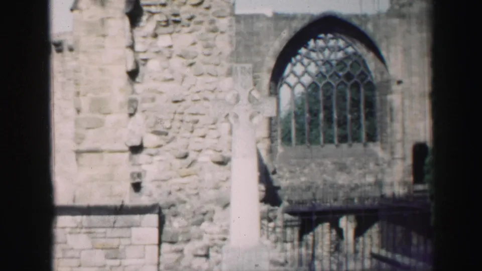 Edinburgh 1952 home-movie frame showing weathered stone ruins, a large arched window, railing, and a pale cross in front.