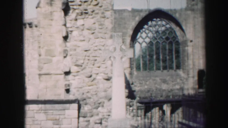 Visitor-shot 8mm view of an Edinburgh church ruin, showing a white cross, rough stonework, and a large arched window.