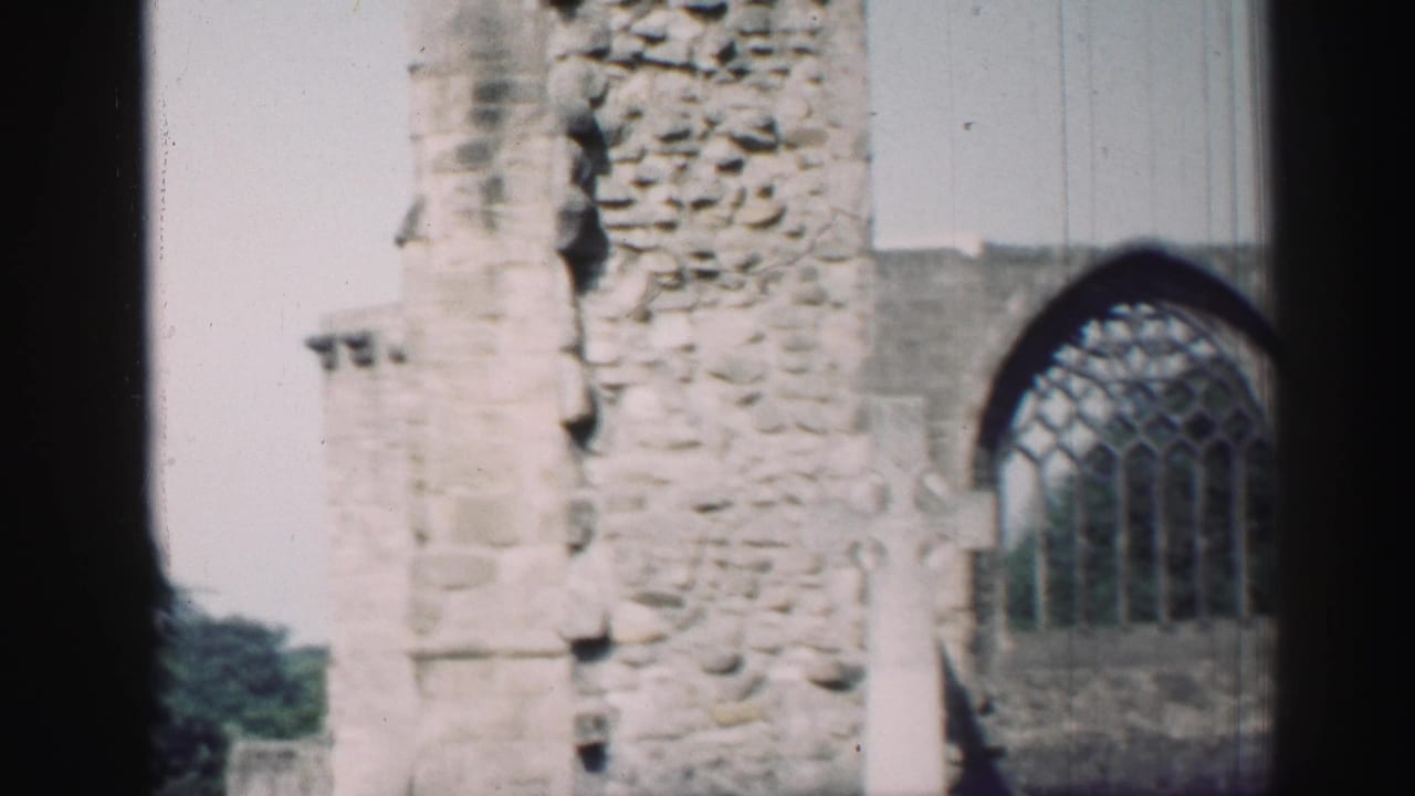 1952 Edinburgh home-movie frame showing weathered chapel stonework and an arched tracery window in bright daylight.