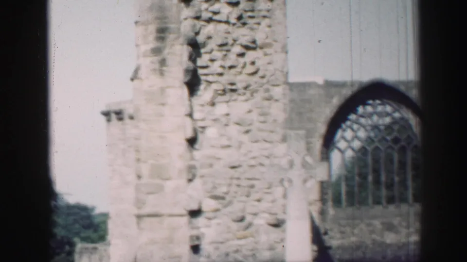 1952 Edinburgh home-movie frame showing weathered chapel stonework and an arched tracery window in bright daylight.