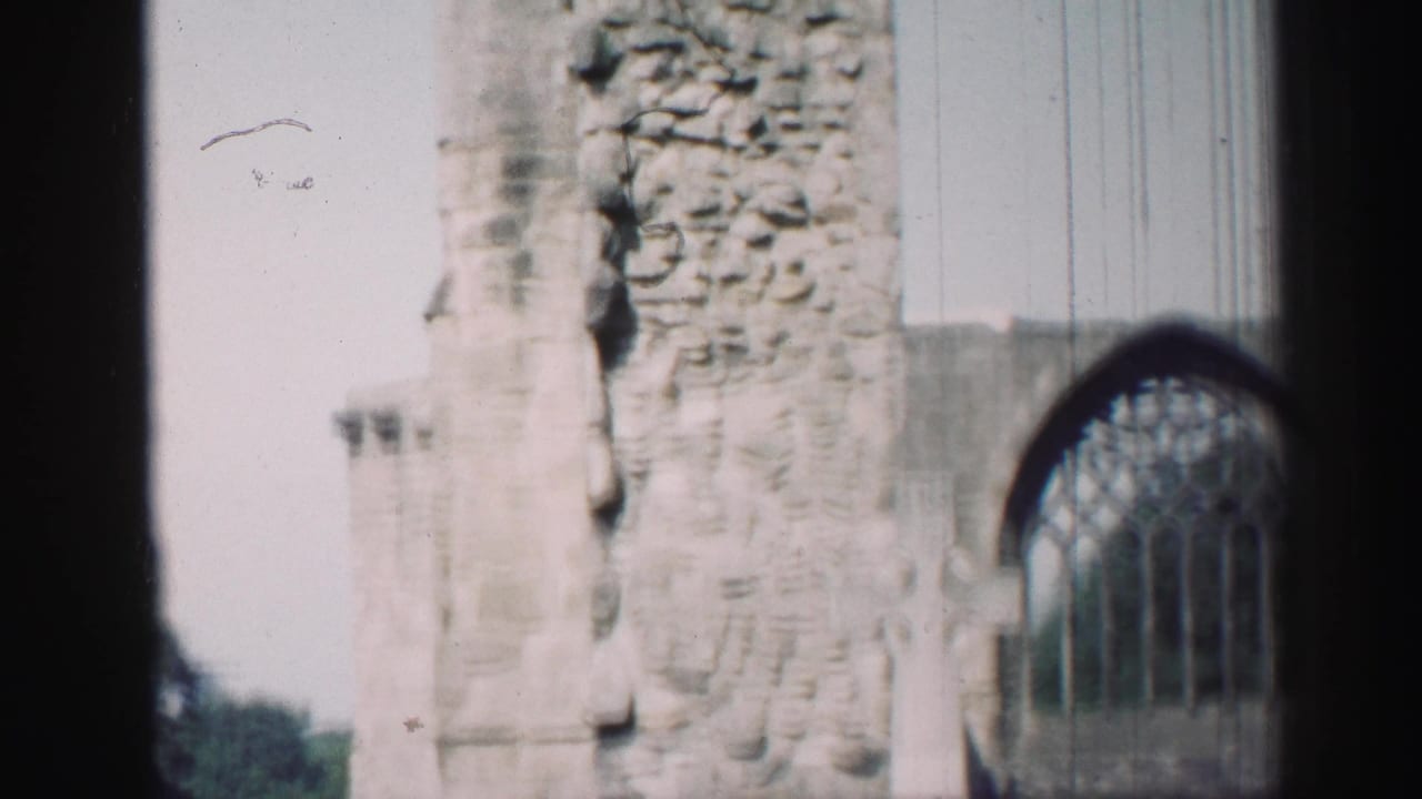 Close view of rough stone wall beside an arched window, partly obscured by dark framing.