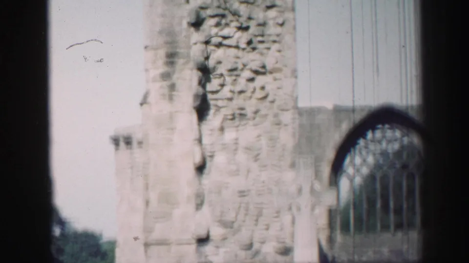 1952 Edinburgh footage frames a chapel ruin with rough stonework, pale sky, and a leaded arched window partly to the right.