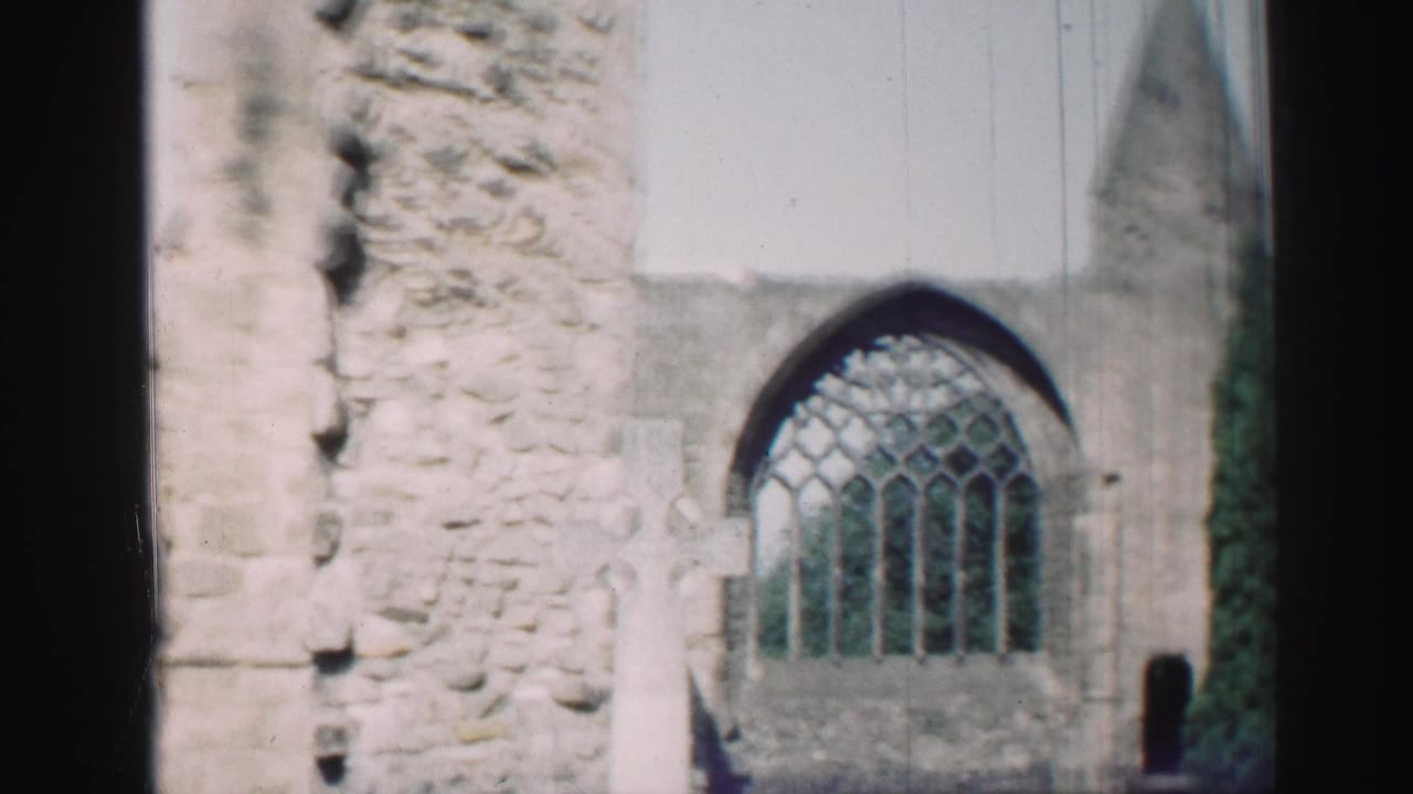 1952 Scotland home-movie frame showing weathered church ruins, a Gothic arched window, pale grave markers, and dark film-edge borders.