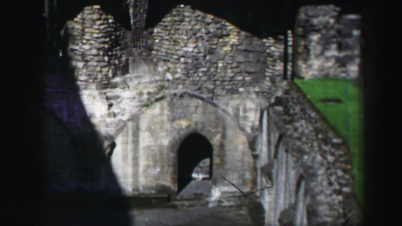 1952 8mm view of Edinburgh stone ruins with an arched entrance, rough upper walls, railing, and grass behind the structure.