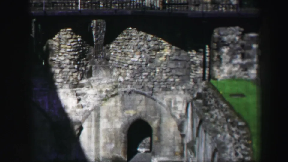 1952 8mm Edinburgh home-movie frame of medieval-looking stone ruins, with a dark archway, worn masonry, and green grass to the side.