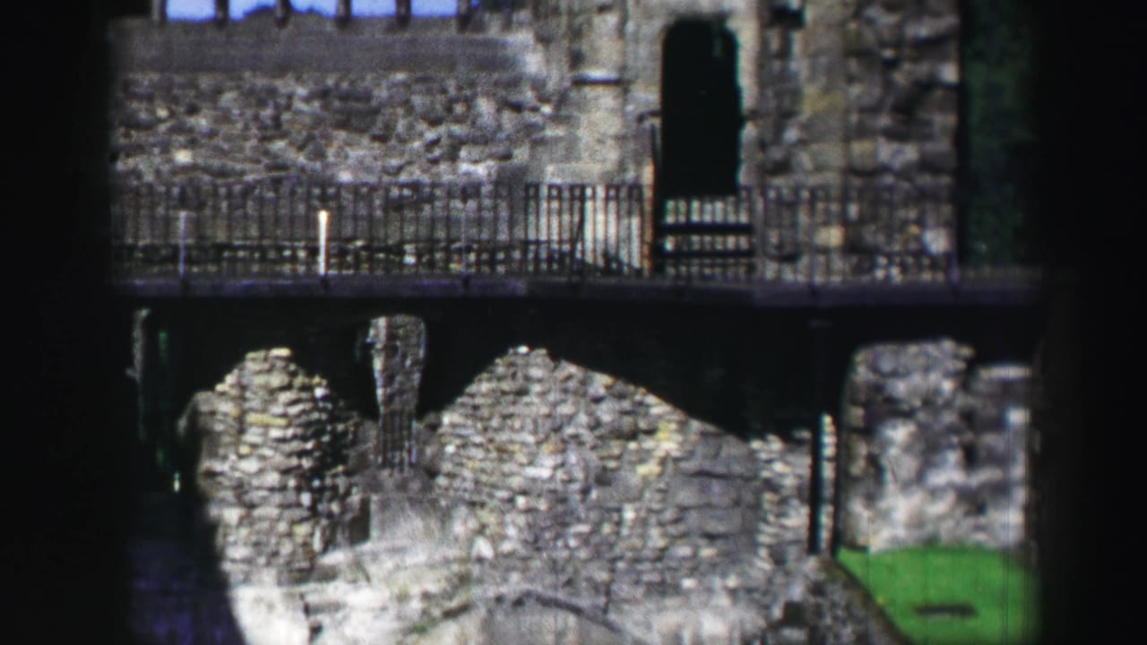 1952 Scotland 8mm frame of weathered stone ruins, metal railings, arched openings, and a dark foreground obstruction.