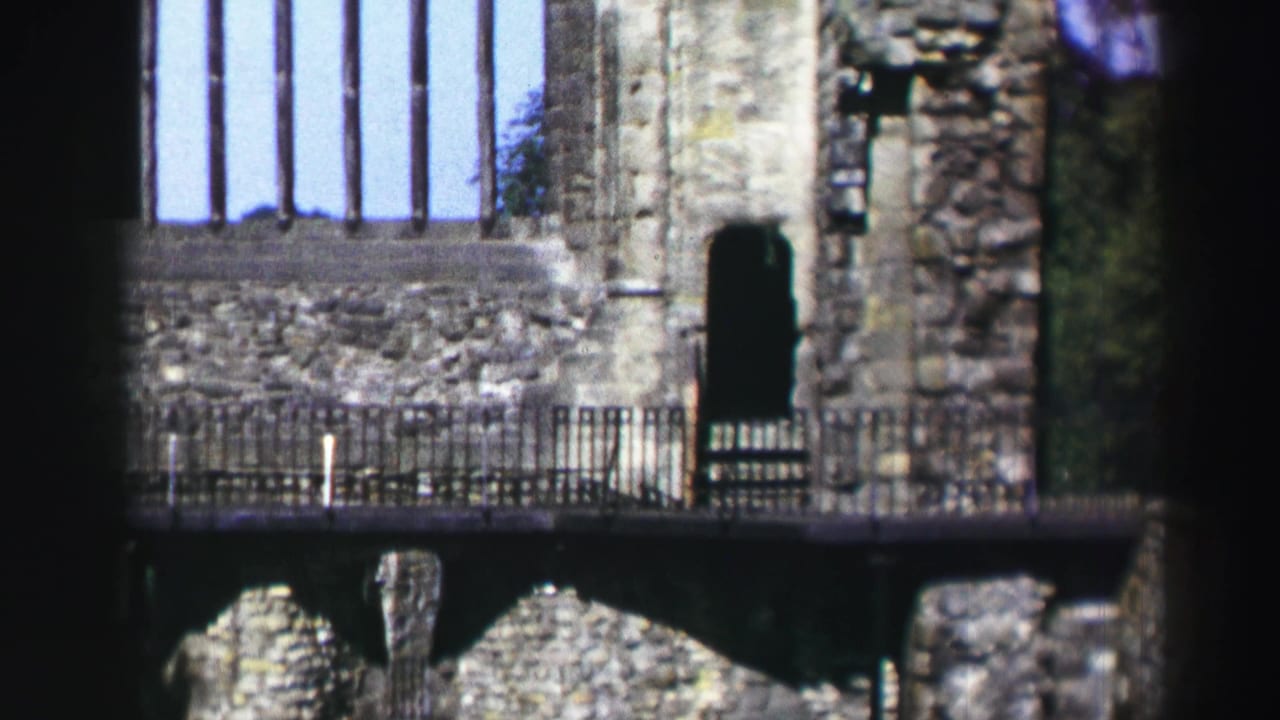 1952 Scotland home-movie frame showing a stone ruin facade with a tall window opening, railings, and dark foreground framing.
