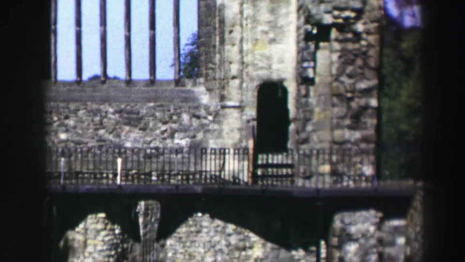 1952 Scotland home-movie frame showing a stone ruin facade with a tall window opening, railings, and dark foreground framing.