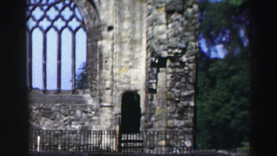 1952 Scotland 8mm view of a weathered ruin wall with a tall arched window, metal railing, and dark frame edges.