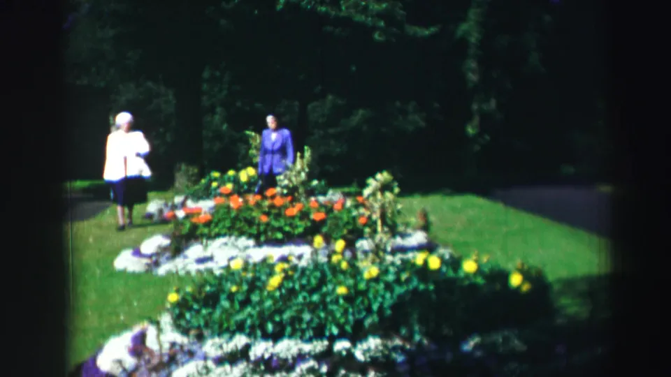 The women remain near the flowerbed in the 1952 Edinburgh garden footage, with bright blooms, lawn, and shaded trees visible.