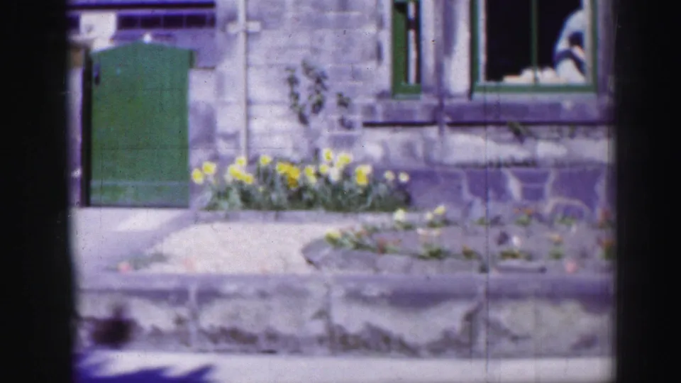 A stone building exterior in the same garden setting shows a green door, window, low wall, and flowers in 1952 Scotland footage.