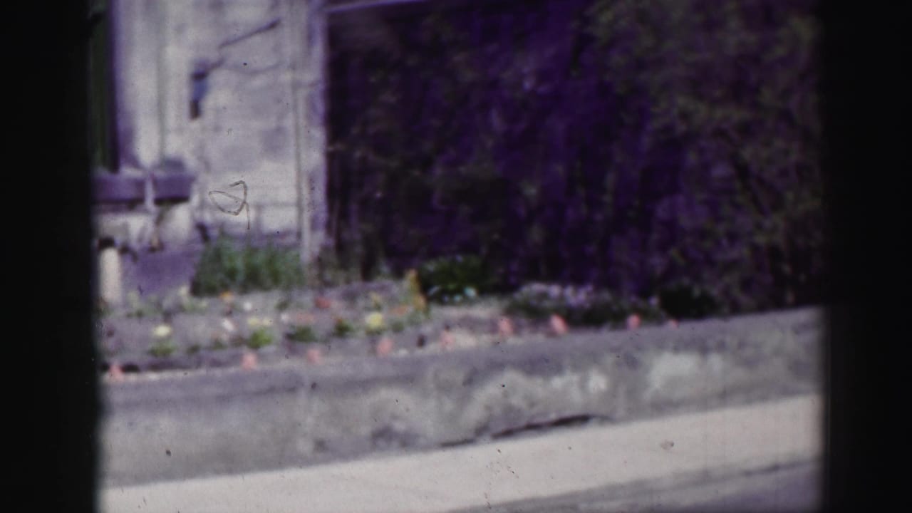 1952 Edinburgh home-movie frame showing a pale stone residential facade, low garden wall, flower bed, and green-trimmed window.