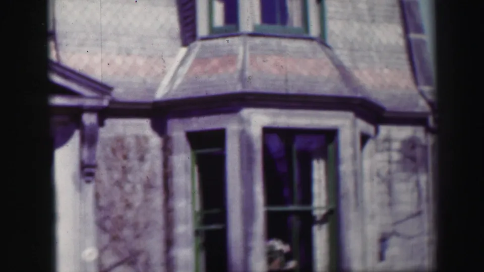 1952 Edinburgh frame showing weathered stonework, green-trimmed windows, a projecting bay or roof edge, and a flower arrangement inside the lower window.