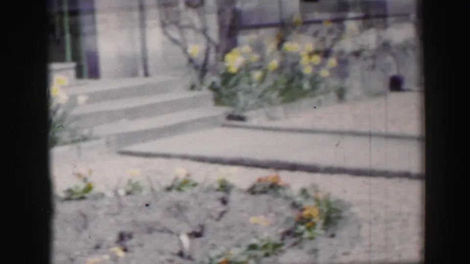 1952 Edinburgh home-movie frame showing porch steps, a gravel path, and soft-focus garden planting near a house exterior.
