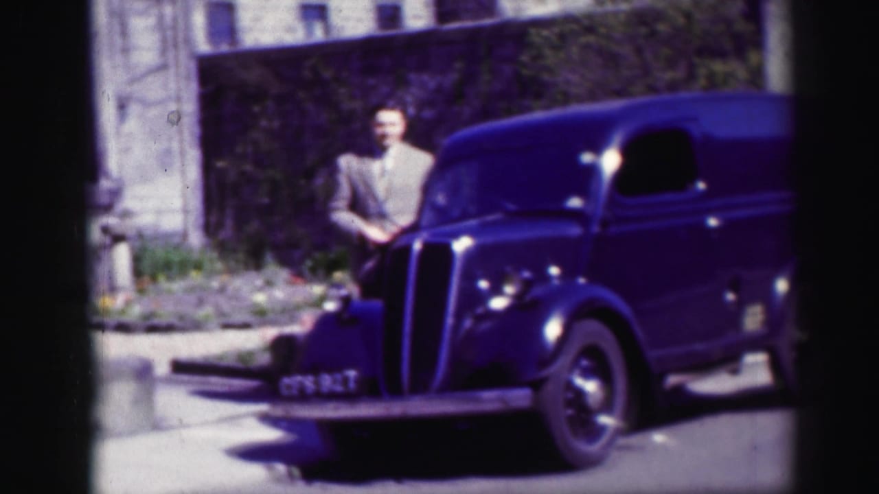 In 1952 Edinburgh footage, a man in a light suit stands by the front of a dark blue delivery-style van outside a stone building.