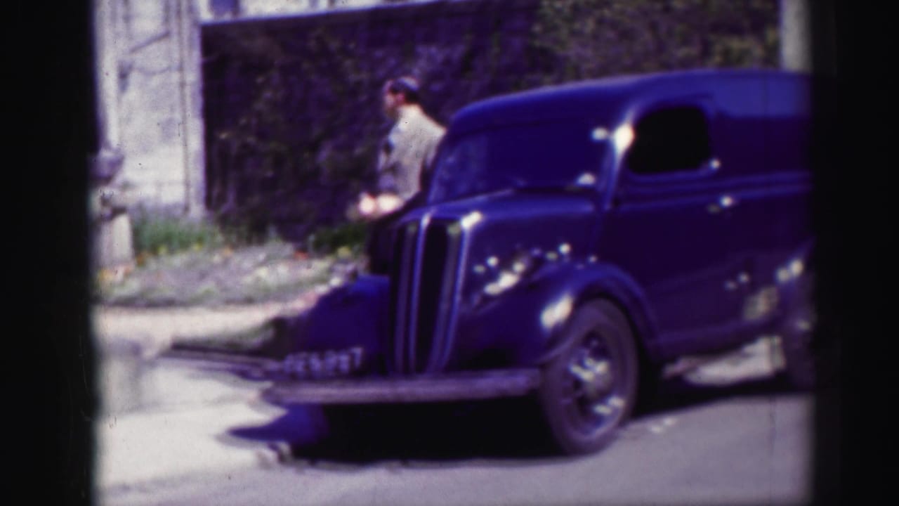 The suited man moves along the pavement near the front of the dark blue van in the Edinburgh street scene.