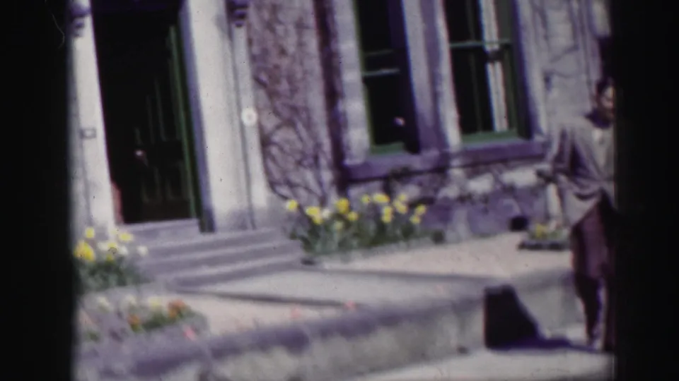 In supported 1952 Scotland footage, a man in a light suit is seen near stone buildings, windows and flower beds along a sidewalk.
