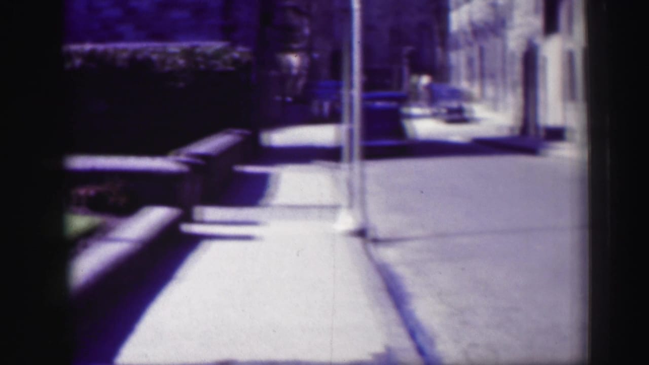 Soft 8mm view along an Edinburgh street, showing a sidewalk, lamppost, stone facades, and parked vintage cars.