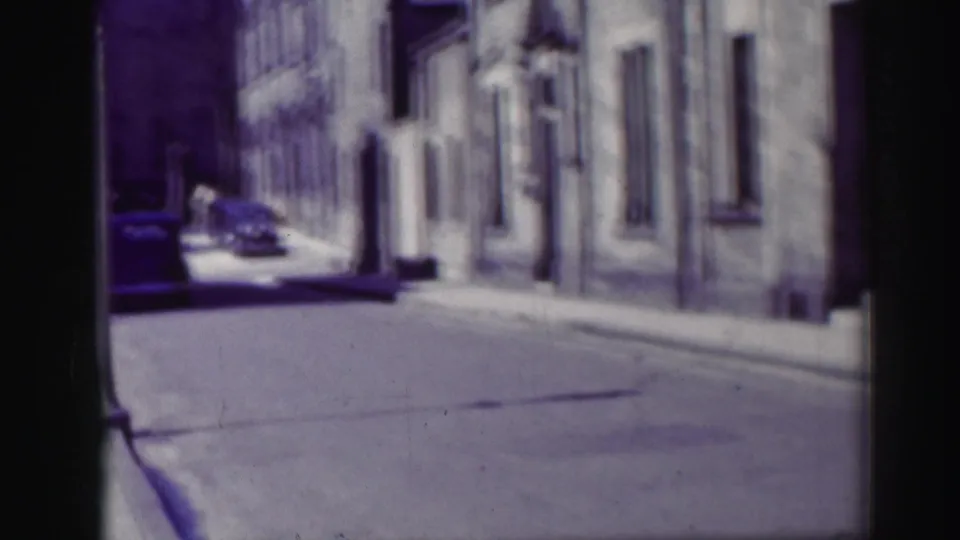 End frame of the 1952 Edinburgh street view, with stone facades, parked cars, a sidewalk, and one distant pedestrian.