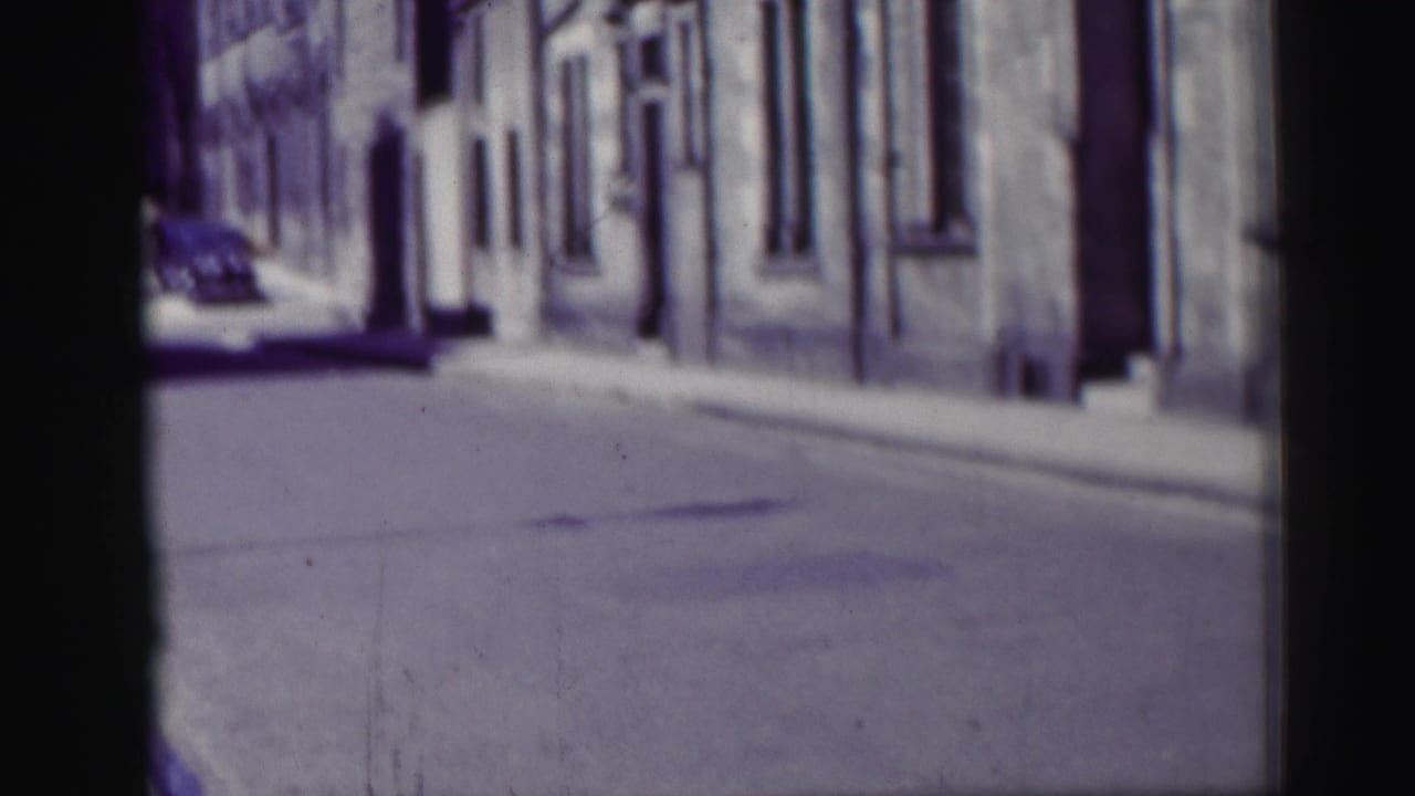 Empty narrow street lined with stone buildings and a distant car.