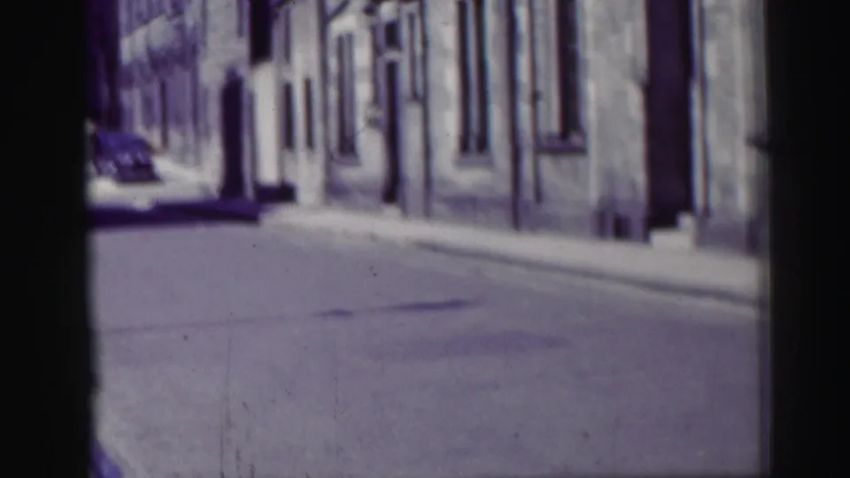 1952 Edinburgh street view with stone facades, an empty roadway and a distant car in soft 8mm focus.
