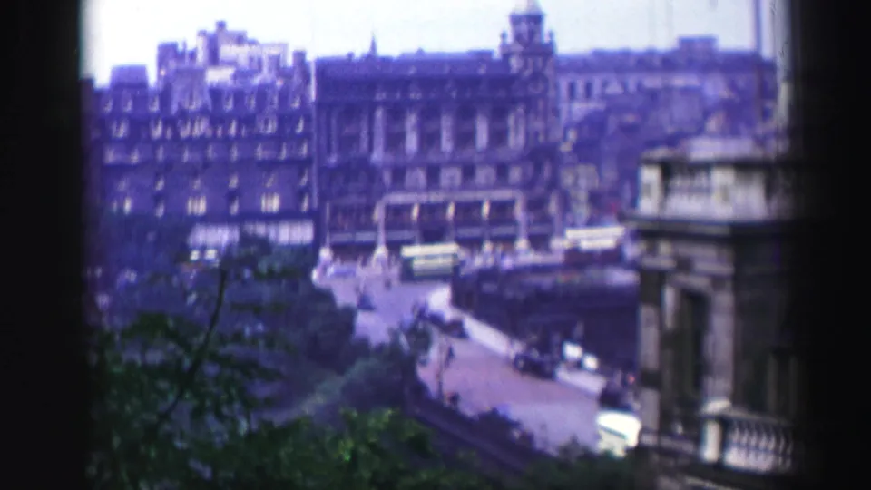 1952 Edinburgh street scene from above, with a bus, cars, multi-story stone buildings, and dark film borders.