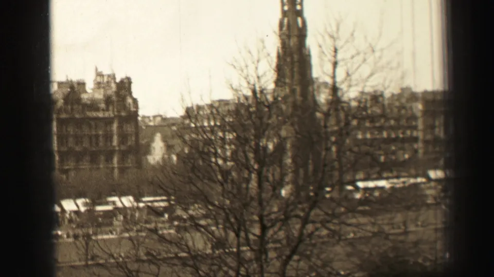 1952 Edinburgh urban view with leafless trees in the foreground, a tall tower, stone buildings, buses, and cars.