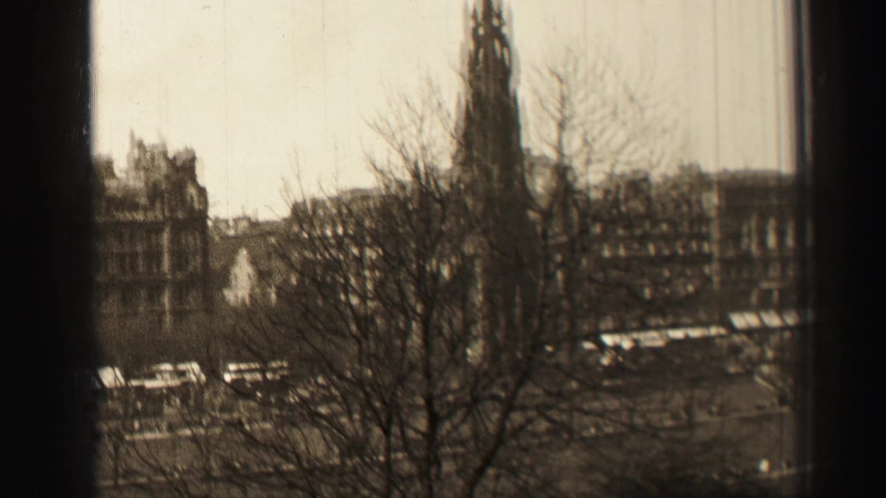 1952 Edinburgh home-movie frame showing bare branches, the Scott Monument area, and city buildings beyond a street.