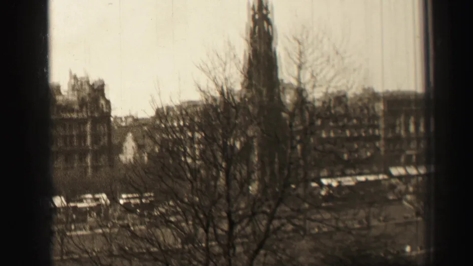 1952 Edinburgh home-movie frame showing bare branches, the Scott Monument area, and city buildings beyond a street.