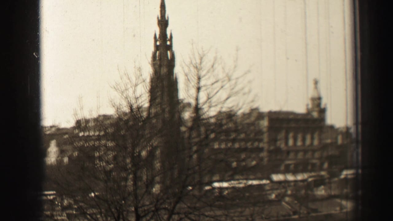 Tall monument rises behind bare branches with city buildings and street activity below.
