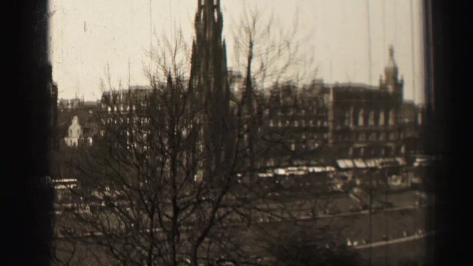 1952 Edinburgh frame with bare branches in front of the Scott Monument, masonry buildings, and vehicles on the street.