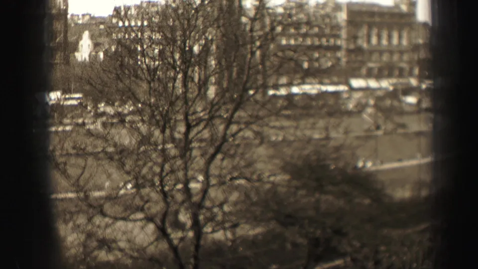 Elevated 1952 Edinburgh street view with bare trees, older commercial buildings, and small vehicles below.