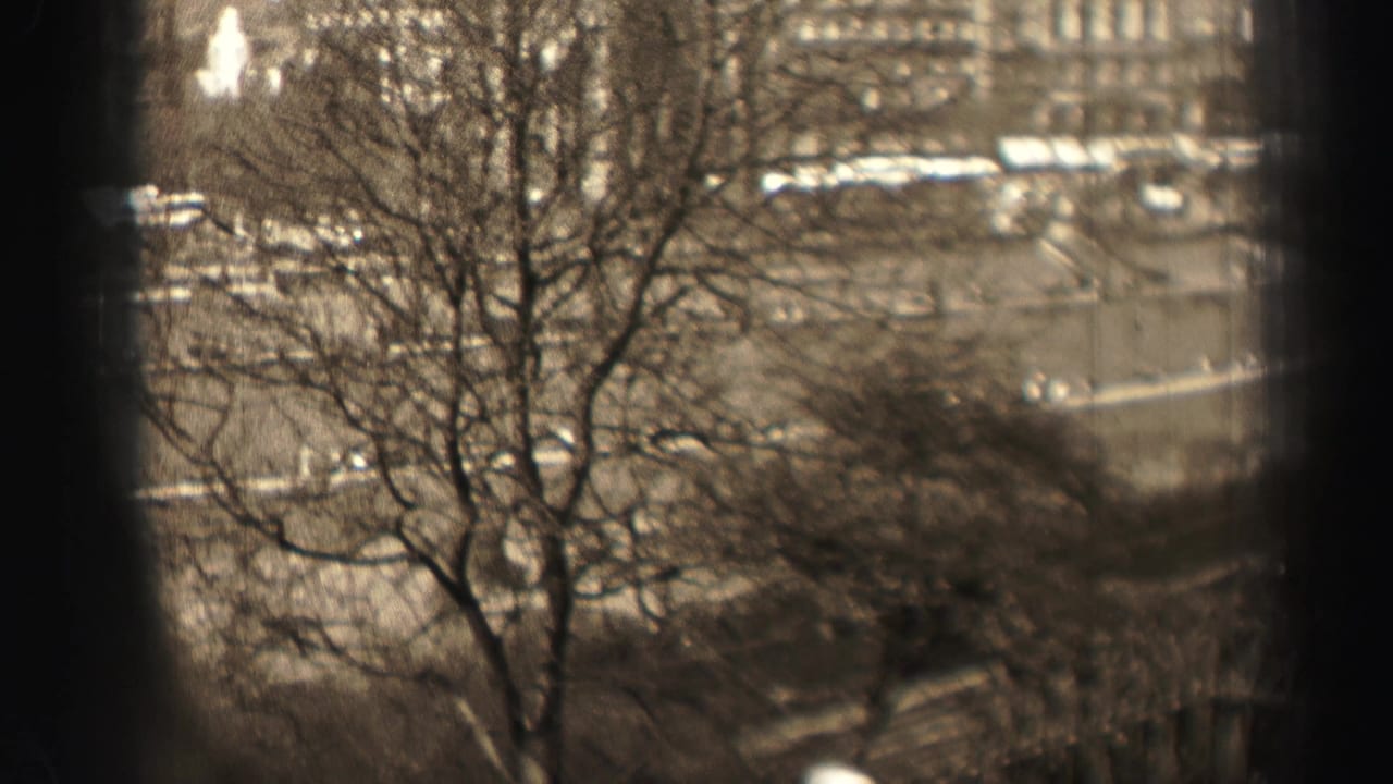 1952 Edinburgh 8mm frame showing bare trees in front of stone city buildings and a broad curving road, seen from an elevated viewpoint.