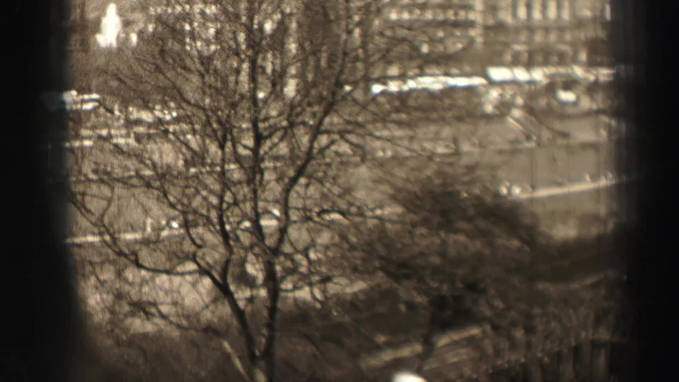 1952 Edinburgh 8mm frame showing bare trees in front of stone city buildings and a broad curving road, seen from an elevated viewpoint.
