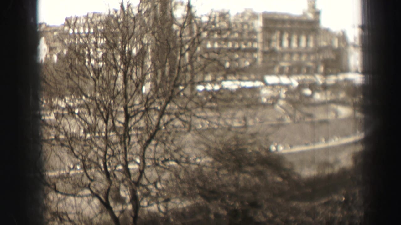1952 Edinburgh street view with leafless trees silhouetted against stone facades and a broad roadway in soft 8mm focus.