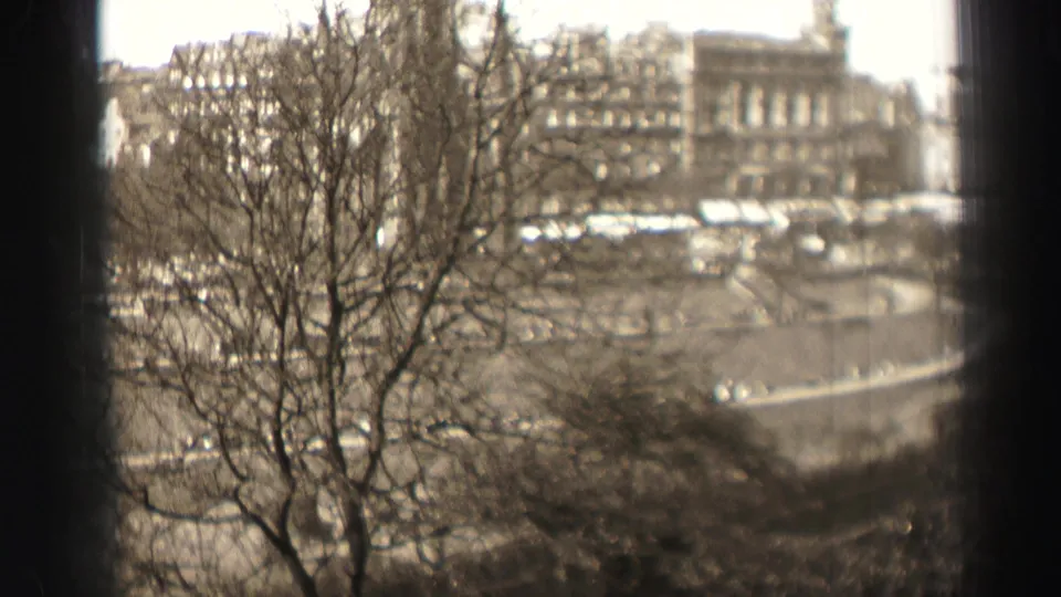 1952 Edinburgh street view with leafless trees silhouetted against stone facades and a broad roadway in soft 8mm focus.
