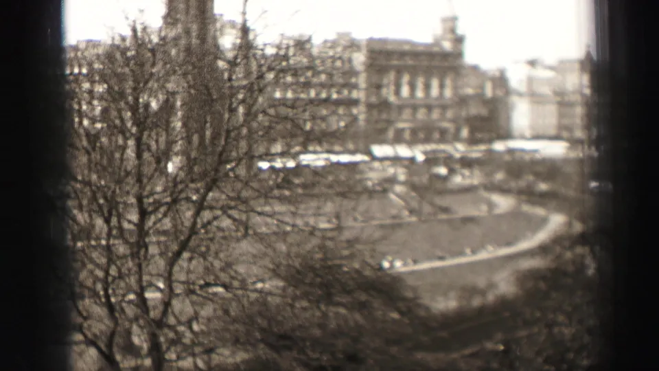 1952 Edinburgh 8mm frame looking past bare branches to a large stone building and curved roadway from a high vantage point.