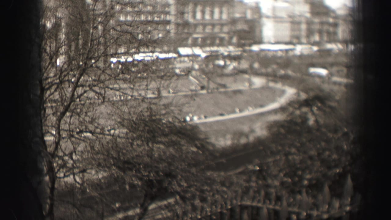 1952 Edinburgh home-movie view from above a park, with bare trees, railings, a curved road, cars, and distant stone buildings.