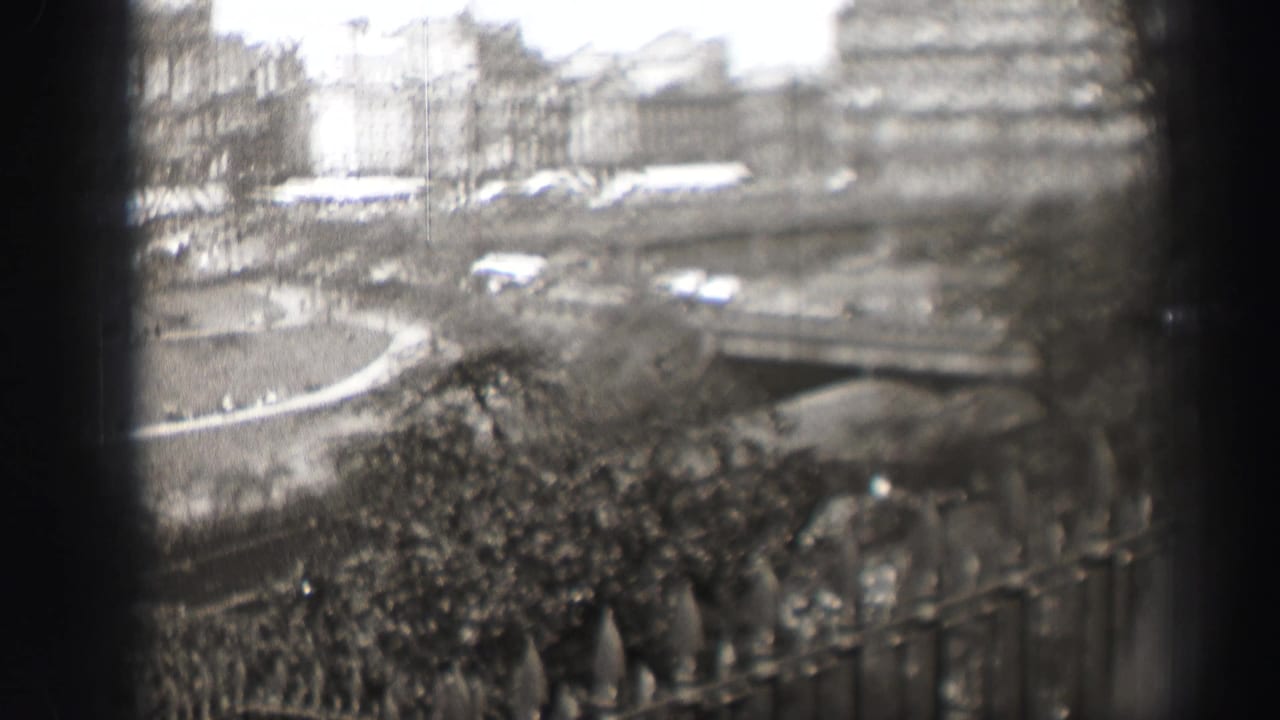 1952 Edinburgh home-movie frame showing a soft elevated city view through a window, with park paths, traffic, trees, and stone buildings.