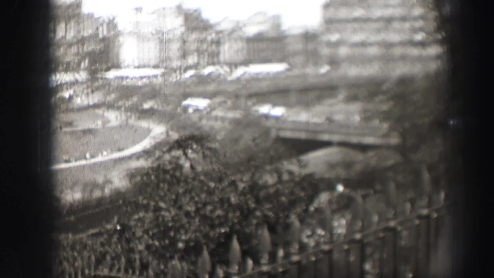 1952 Edinburgh home-movie frame showing a soft elevated city view through a window, with park paths, traffic, trees, and stone buildings.