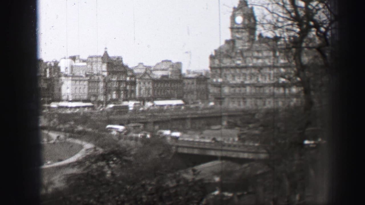 Black-and-white view of a bridge, traffic, stone buildings, trees, and a clock tower beyond the street.