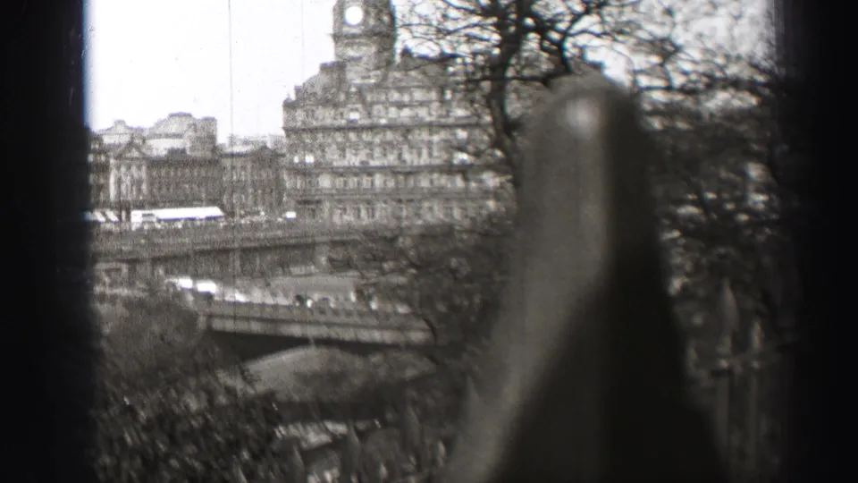 1952 Edinburgh city view with bridge traffic, park trees, stone buildings, and a clock tower partly obscured by foreground railing.