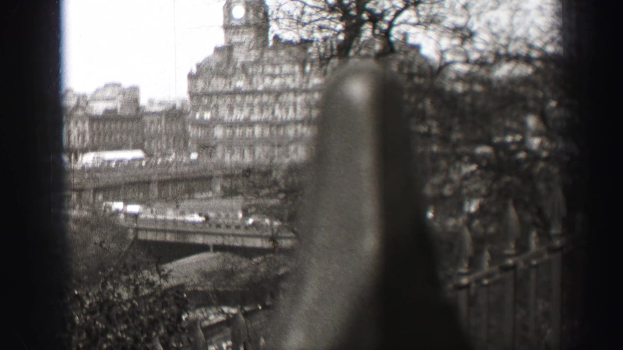 1952 Edinburgh home-movie frame looking past out-of-focus iron railings toward stone buildings, bare trees, and a city bridge.