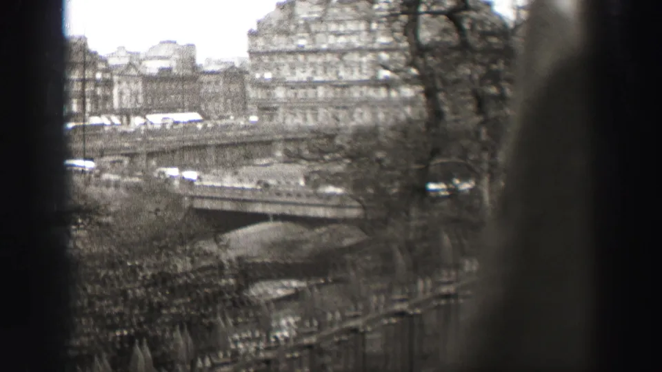 1952 Edinburgh view framed by dark vertical obstructions, with a bridge, street traffic, stone facades, and leafless trees visible.