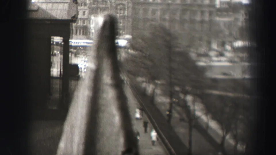 1952 Edinburgh street scene from above, partly obscured by a soft foreground railing, with pedestrians and vehicles along a tree-lined road.