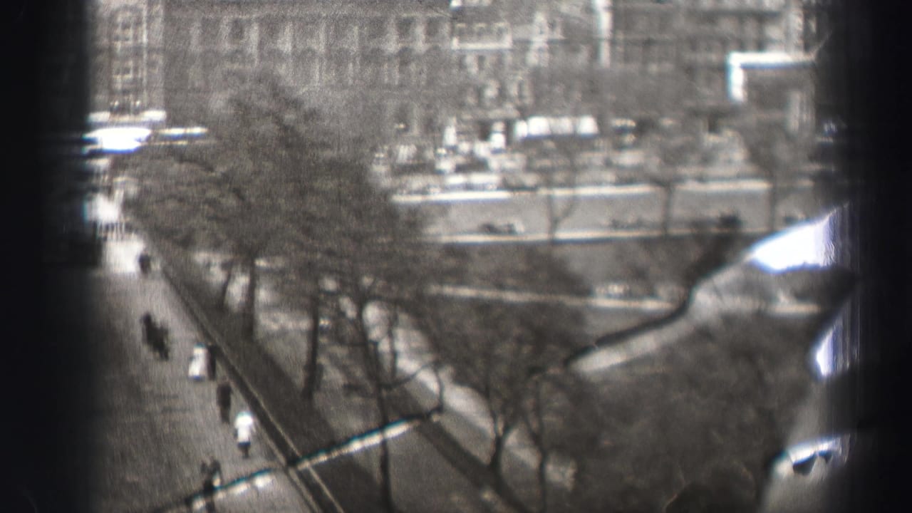 1952 Edinburgh home-movie frame from above, showing a tree-lined street with pedestrians and traffic partly obscured by dark vertical foreground shapes.